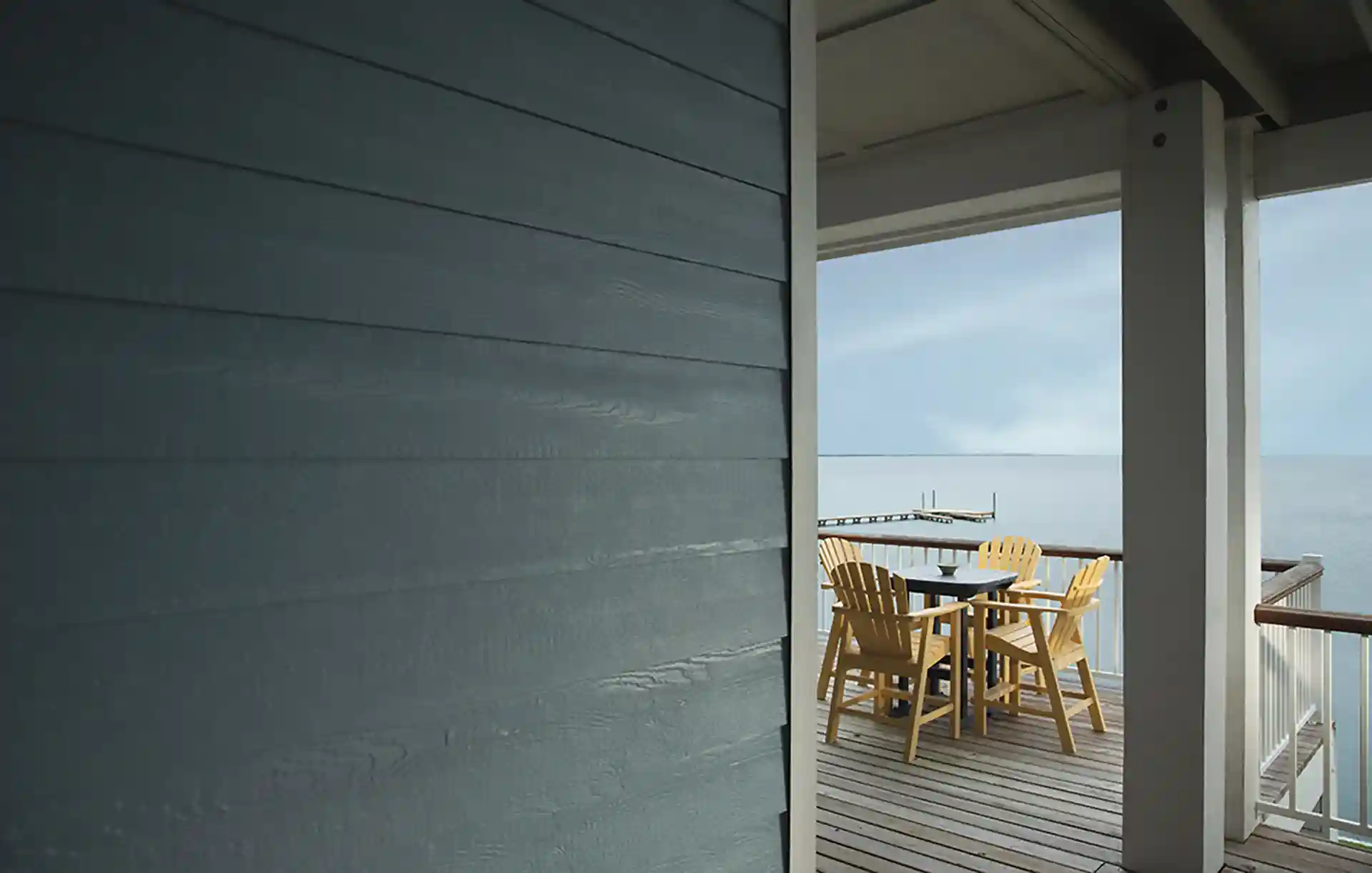 Waterfront deck with yellow Adirondack chairs and a table overlooking the ocean and a dock.
