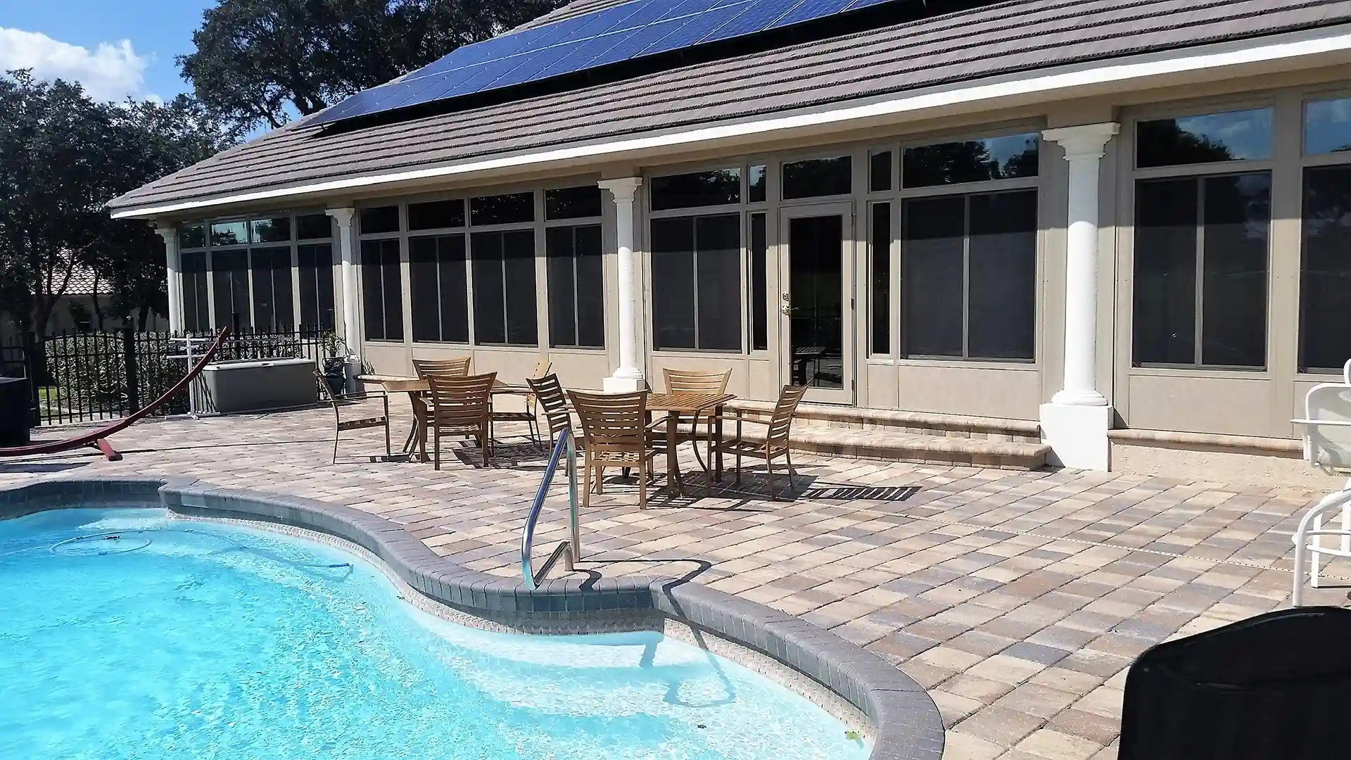 Screened-in patio with columns overlooking a pool and outdoor seating area.
