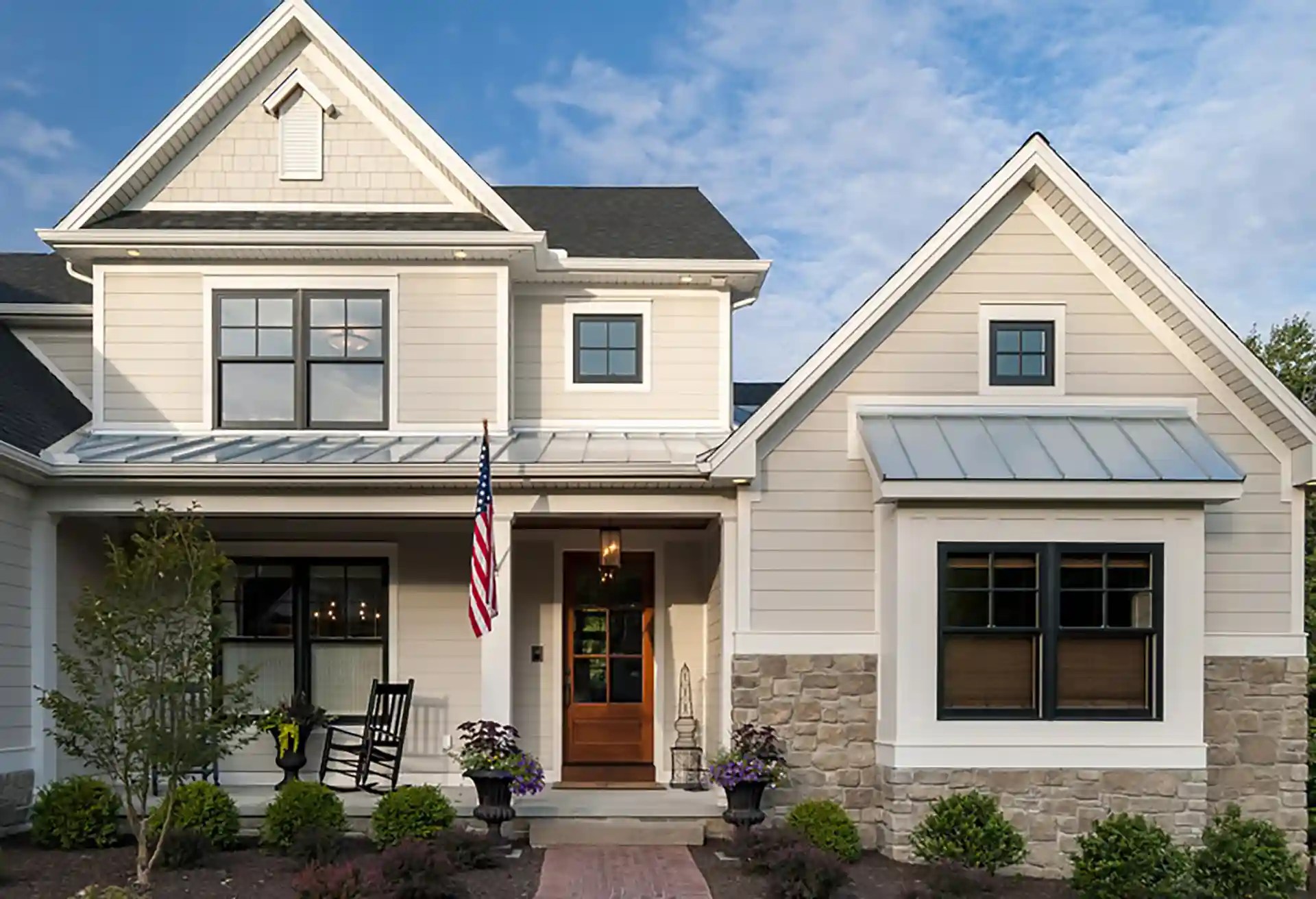 Elegant modern farmhouse with light-colored siding, stone accents, a welcoming front porch, and black window trim.
