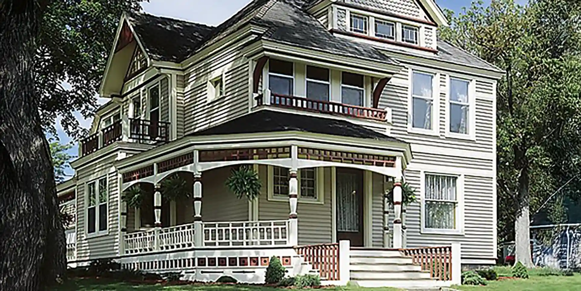 Victorian-style home with a wraparound porch, decorative railings, and a gabled roof. 