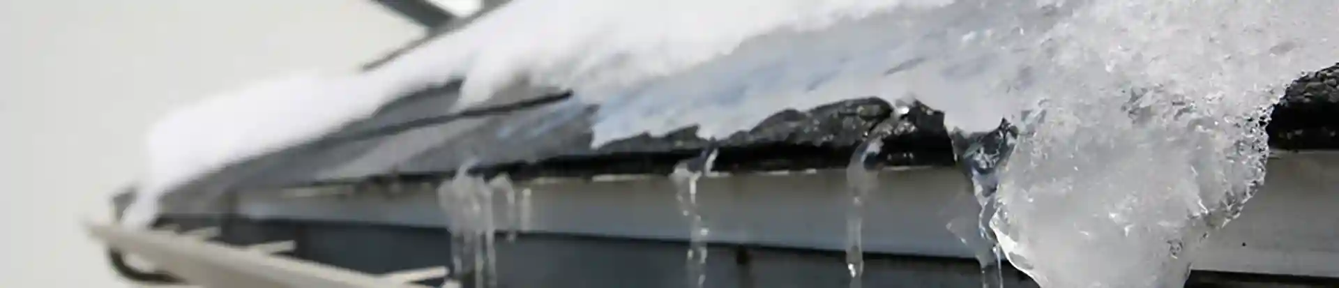 Ice and snow buildup on a roof with icicles forming along the gutter.
